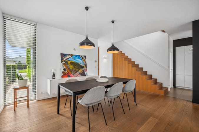 Stijlvolle eetkamer met houten vloer en moderne verlichting, gefotografeerd voor verkoop van residentieel vastgoed.