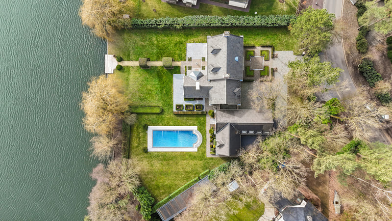 Luchtfoto van luxe woning aan het water met zwembad en tuin, gemaakt voor vastgoedmarketing.